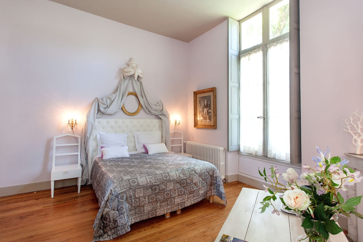 Un dormitorio con una cama grande, una mesita de noche, un radiador y una ventana con cortinas.