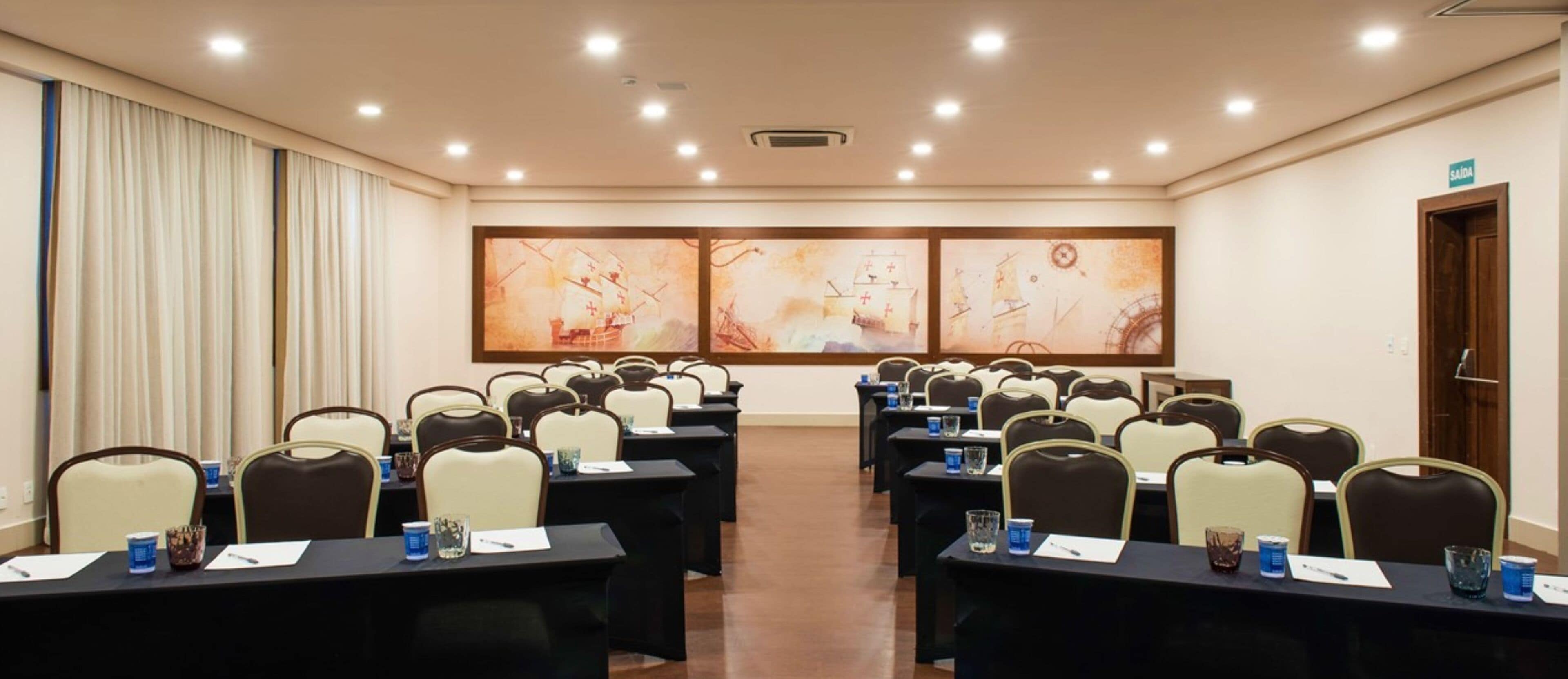 A conference room with rows of tables and chairs, a large abstract painting on the wall, and a door labeled "SAIDA".