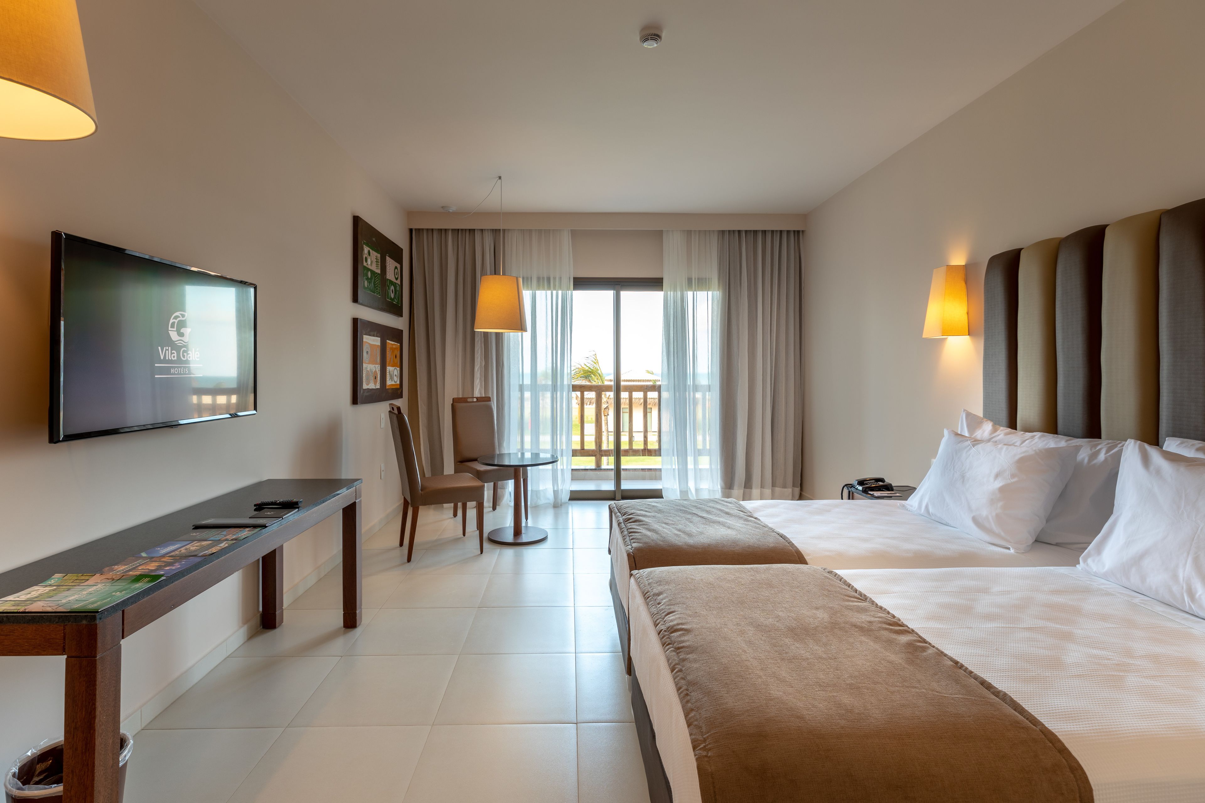 A hotel room with a TV, a desk with a chair, a bed, and a view of the outdoors.