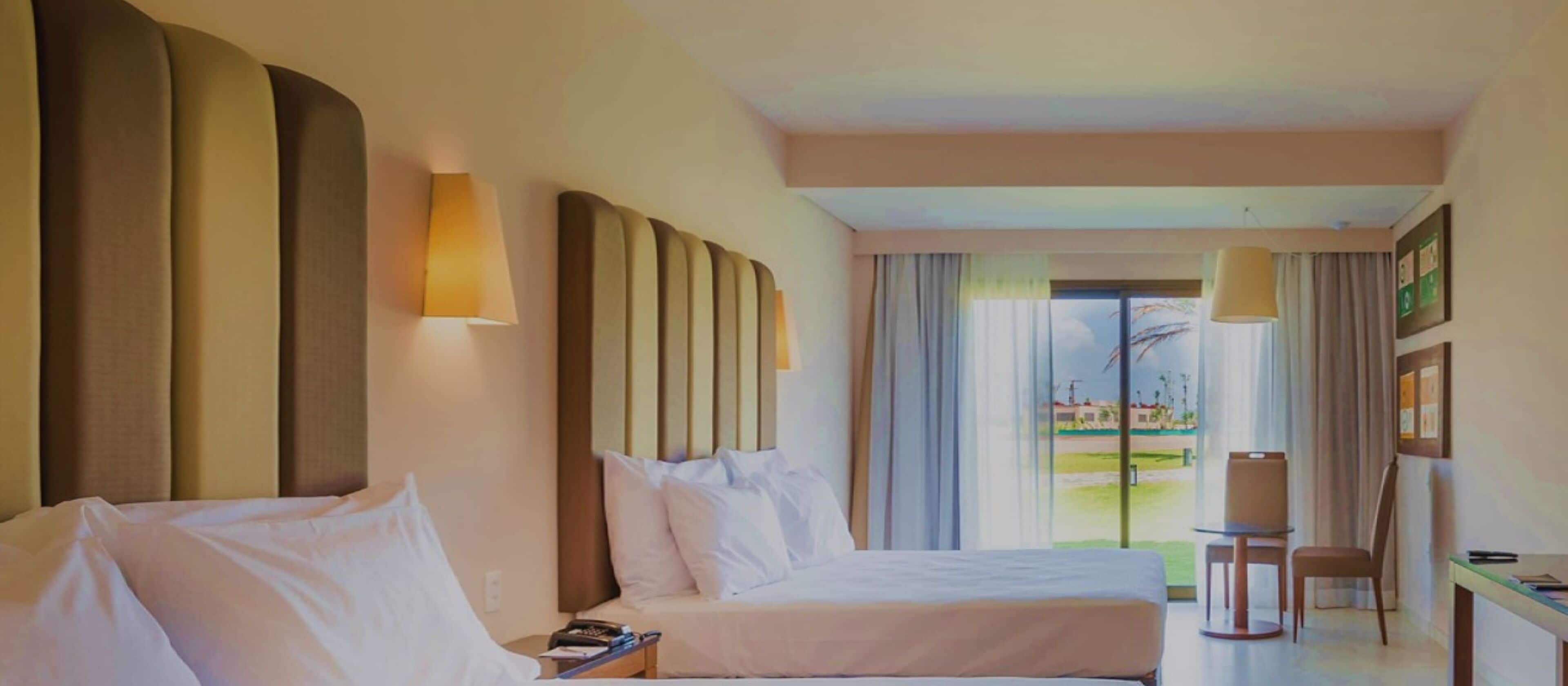 A hotel room with two beds, a desk, and a view of the outdoors.