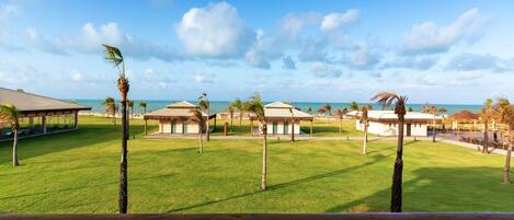 Un resort con varias construcciones de techo de paja, un césped y una vista despejada del océano.