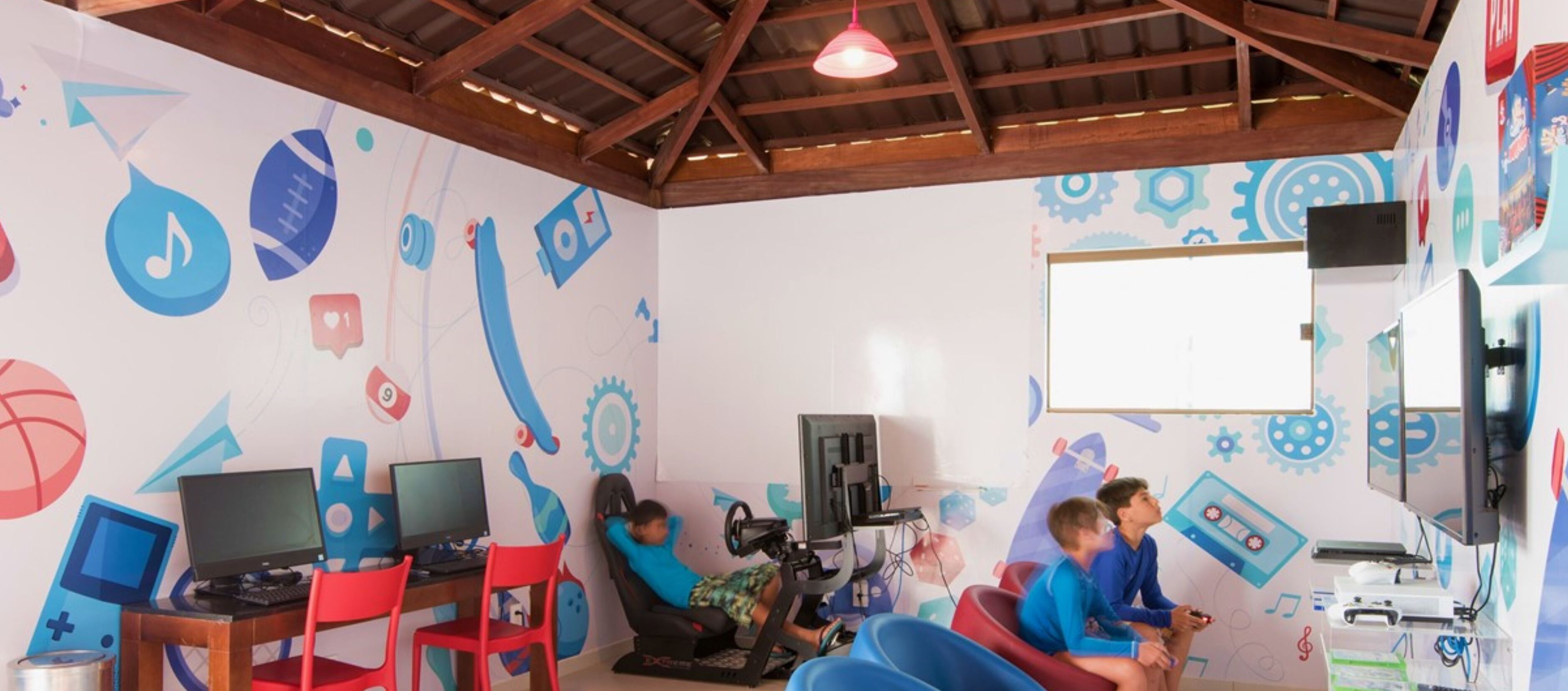 Una habitación con techo de madera, una pizarra y una pared con gráficos educativos. Hay dos escritorios con computadoras y sillas.