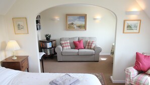 Un dormitorio con una cama, un sofá gris, un sillón pequeño, una estantería y un cuadro en la pared.
