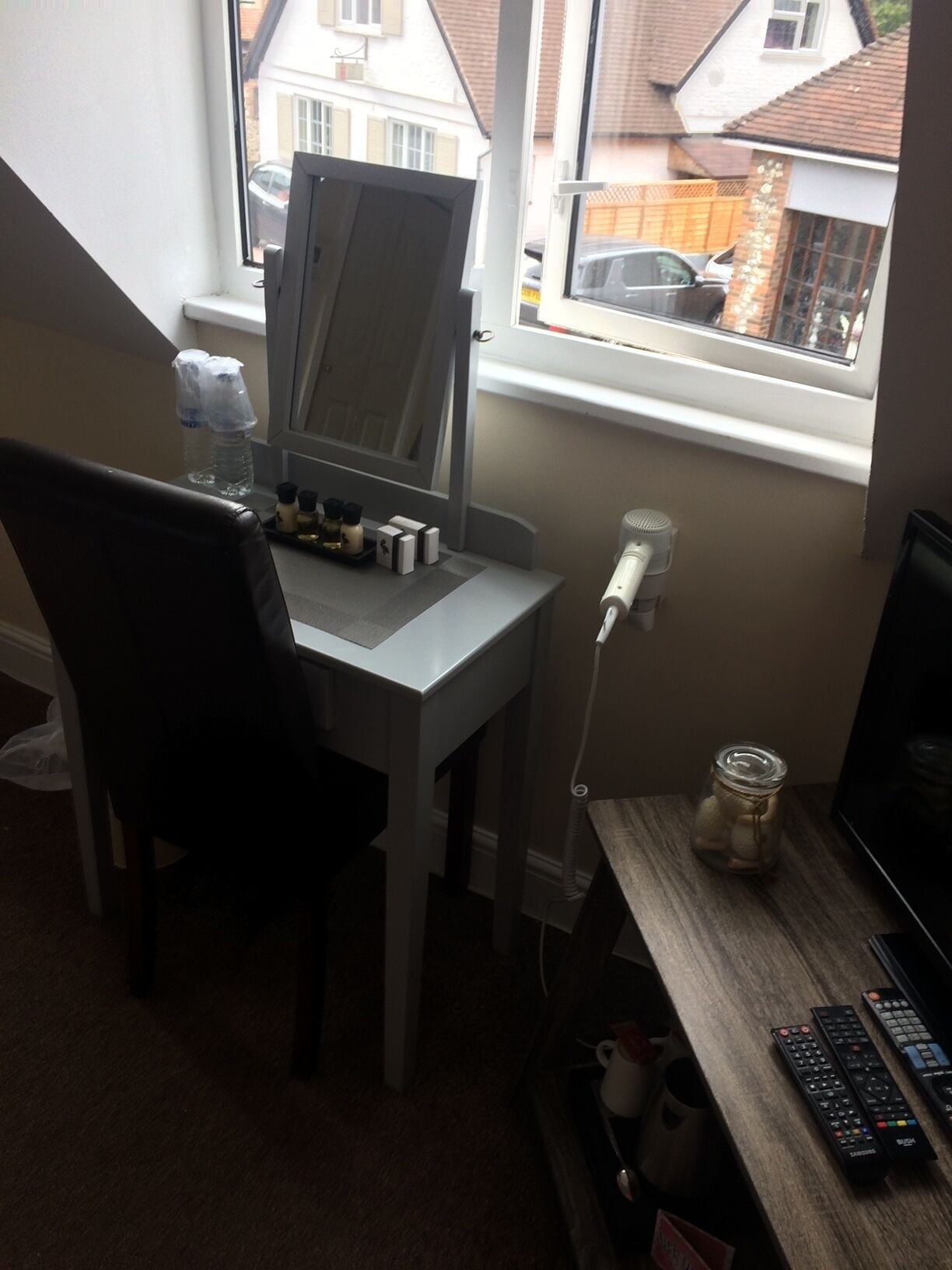 Een kleine kantoorruimte met een bureau, stoel, computer en een raam met uitzicht op huizen.