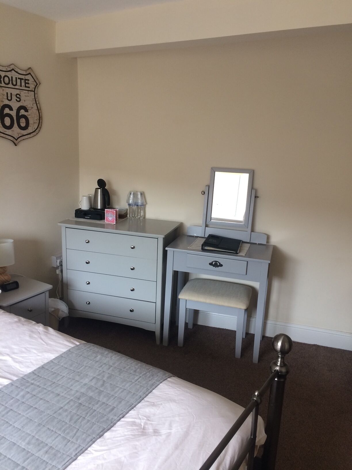 Una habitación de hotel con una cama, un escritorio con una computadora, un aparador y un letrero en la pared que dice "ROUTE US 66".
