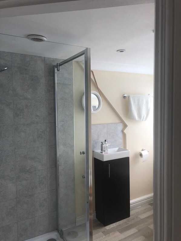 A modern bathroom with a glass shower enclosure, a white sink, and a towel rack.