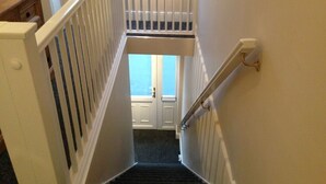 Un escalier étroit avec une rampe blanche, menant à une porte située en haut.