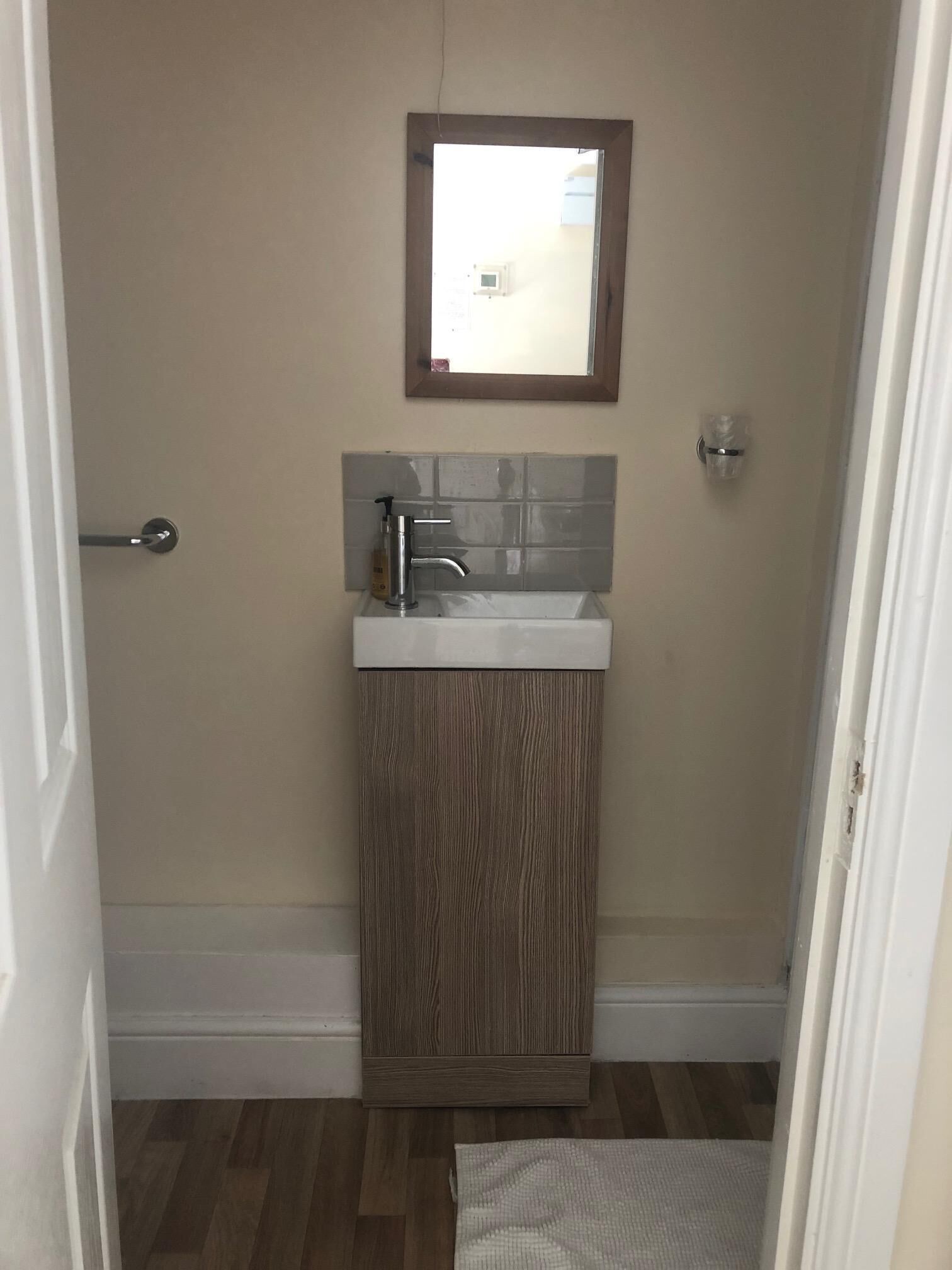 Een badkamer met een houten kastje, een wit wastafel en een spiegel erboven.