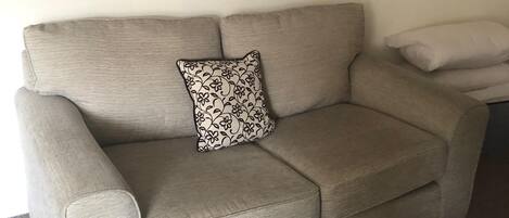 A beige sofa with a floral pillow, a plain pillow, and a black and white cityscape painting above.