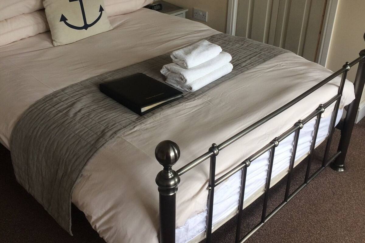 A neatly made bed with a metal frame, a pillow with an anchor design, and a folded towel on the bed.