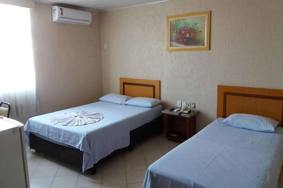 A hotel room with two single beds, a small bedside table with a phone, and an air conditioning unit on the wall.