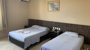 A hotel room with two single beds, a nightstand with a phone and remote controls, an air conditioning unit, and a painting on the wall. - Hotel Central (Porto Velho)