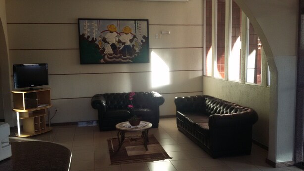 A living room with a black leather sofa, a television on a wooden stand, and a painting on the wall. - Hotel Central (Porto Velho)