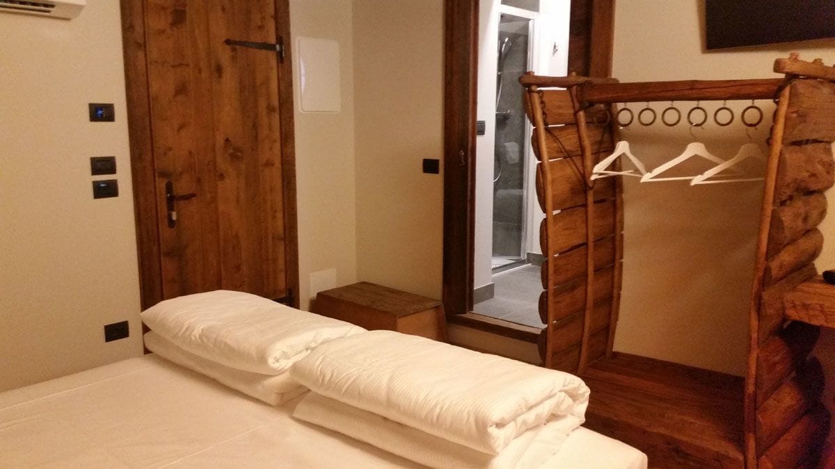 A bedroom with a wooden wardrobe, a bed with white bedding, and a wooden coat rack with hangers.