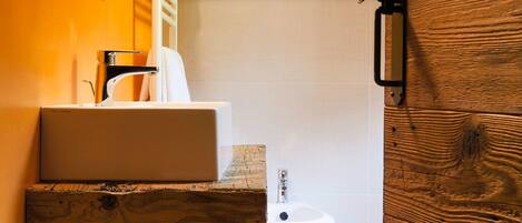A bathroom with a wooden vanity, a white sink, and a bidet.