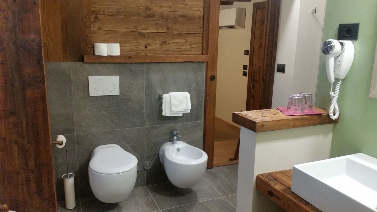 Un baño con bidé, inodoro, lavamanos y secador de pelo en la pared.