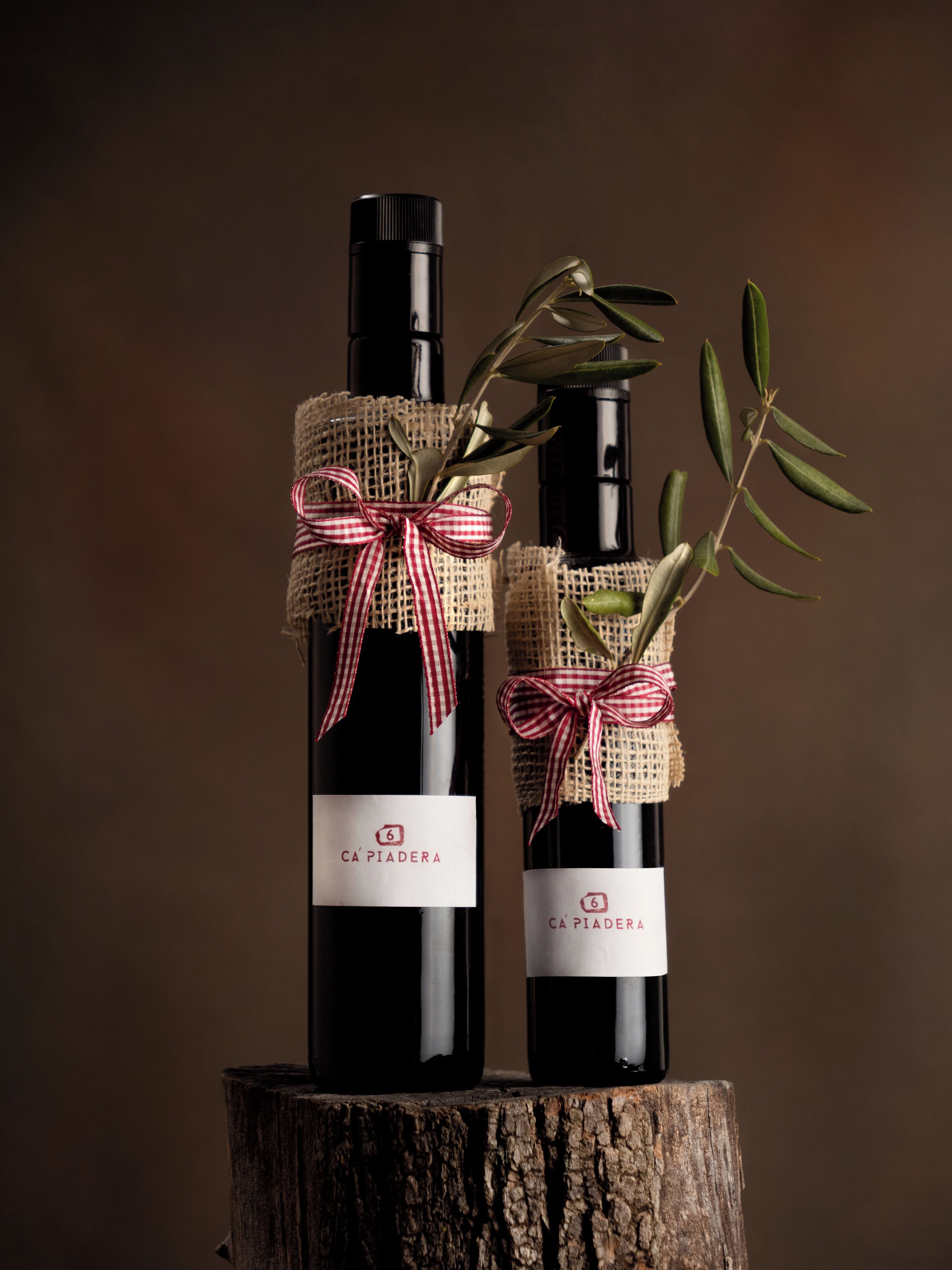 Two bottles of wine with corkscrews and ribbons tied around them, placed on a wooden stump.