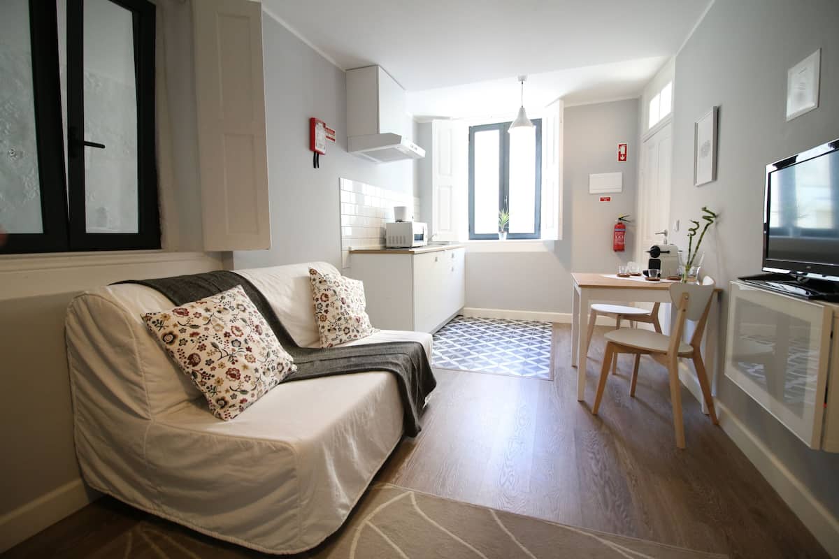 Un espacio habitable compacto con sofá, una pequeña mesa de comedor, televisión y kitchenette.