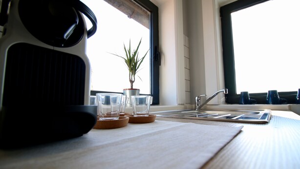 Een keukentafel met een waterkoker, glazen en een potplant.