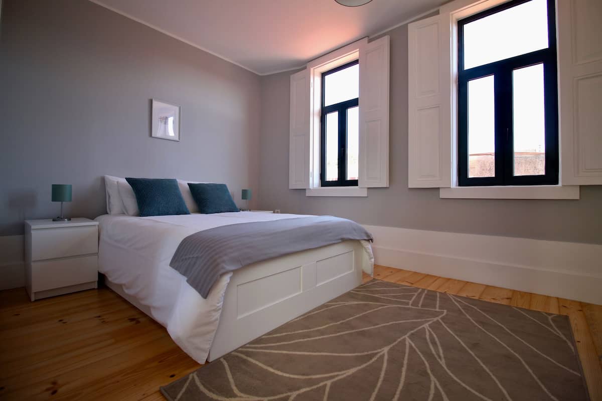Un dormitorio con cama, mesitas de noche, una ventana y una alfombra.