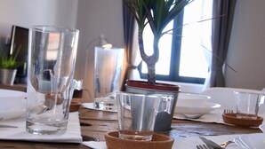 Een houten eettafel met helder glaswerk, een potplant en een kaars in een glazen houder.