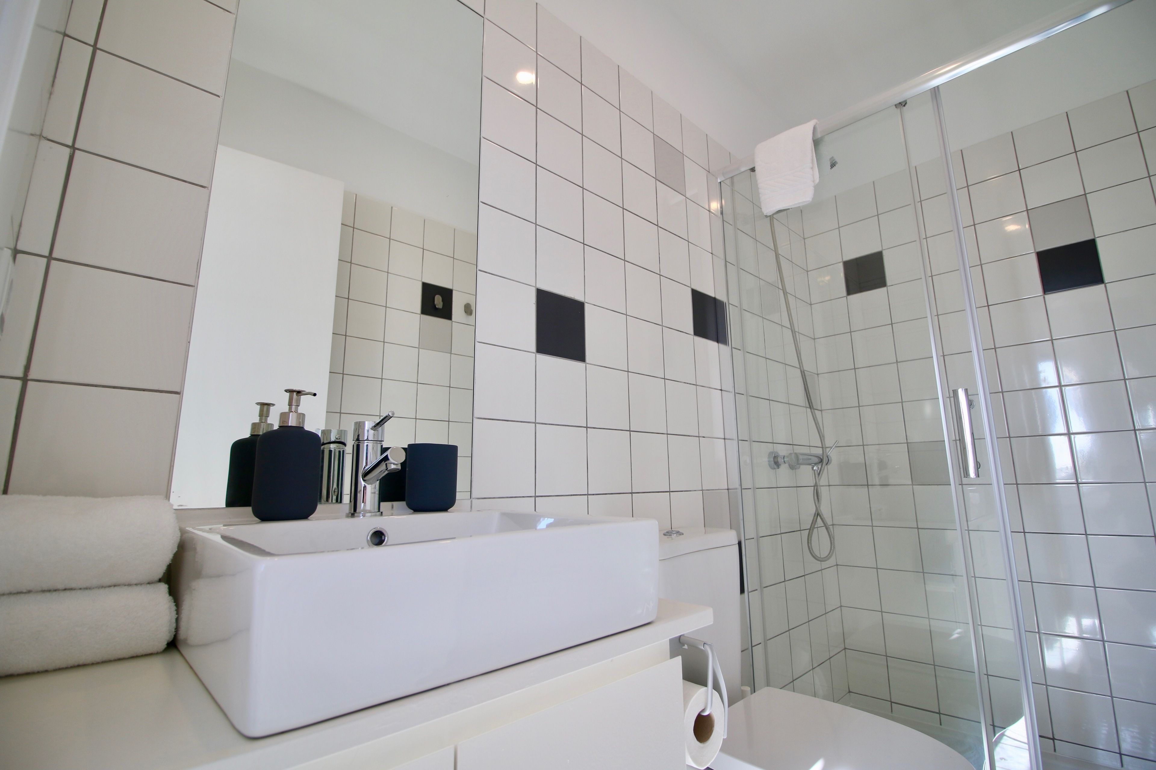 Ein modernes Badezimmer mit einem großen, weißen Waschbecken, einem Spiegel und einer gläsernen Duschkabine.