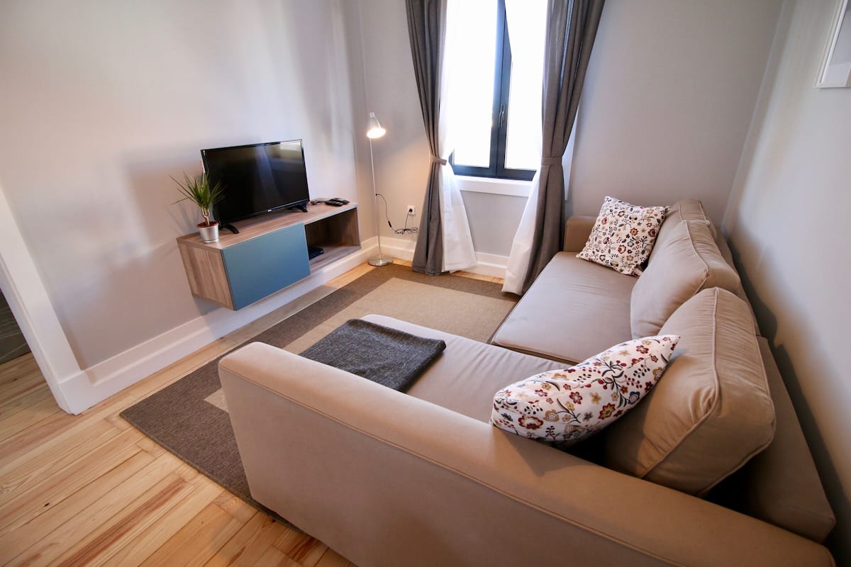 Una sala moderna con un sofá, un televisor de pantalla plana, una lámpara de pie y una ventana con cortinas.