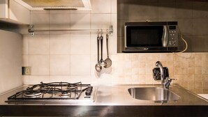 A kitchen with a gas stove, a microwave, a sink, and hanging utensils. - Mono Verde (Turin)