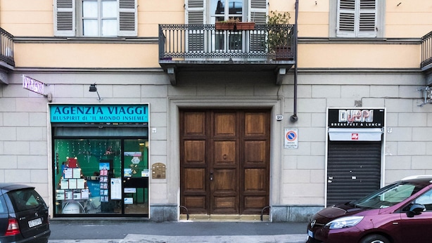 A building with a ground-floor shop, a wooden door, and a parked car. - Mono Verde (Turin)