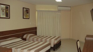 Camera d'albergo con due letti, una testiera in legno, una scrivania e una finestra con tende.