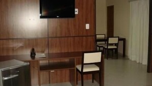 Camera d'albergo con parete rivestita in legno, una TV a schermo piatto sopra una scrivania in legno, un piccolo frigorifero e una zona pranzo con sedie e tavolo.