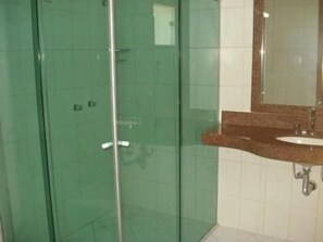 A bathroom with a glass-enclosed shower, a sink with a marble countertop, and a mirror above the sink. - Flamboyant Suite Hotel (Porto Velho)