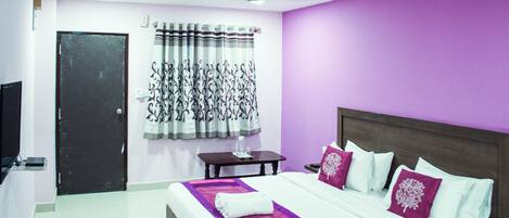 A hotel room with a bed, a nightstand, a TV, a window with curtains, and a door.