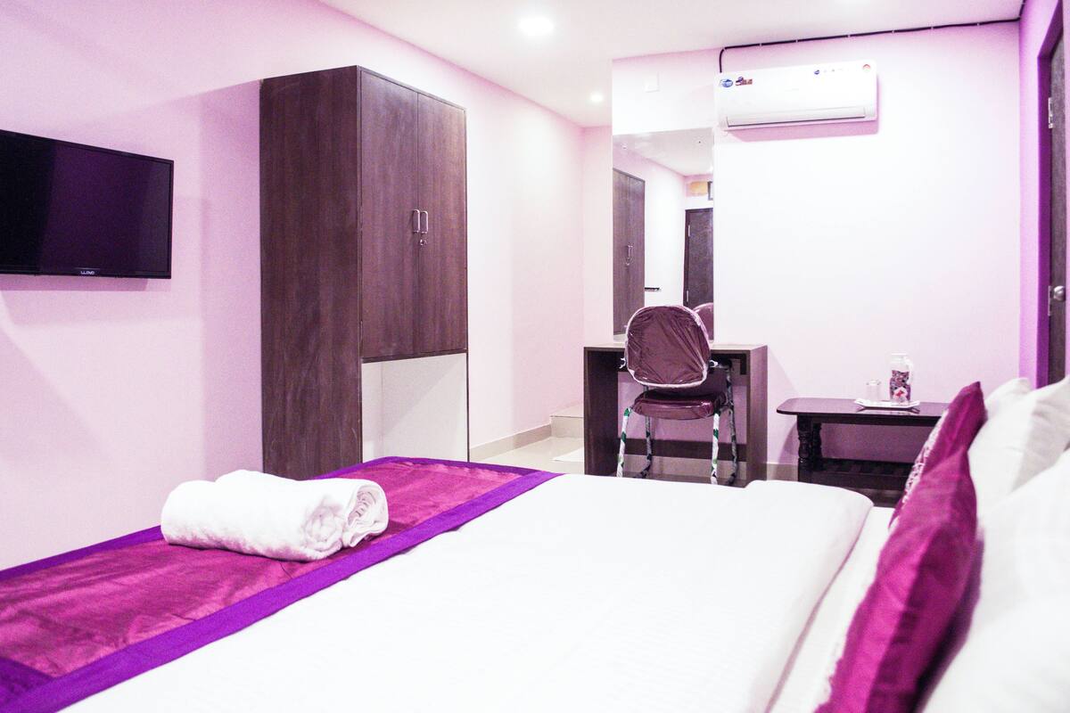 A hotel room with a bed, a desk, a chair, and a television on the wall.