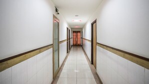 A long, narrow hallway with white walls and a tiled floor, leading to a door at the end. - OYO 8501 Abhimaani Comforts (Bengaluru)