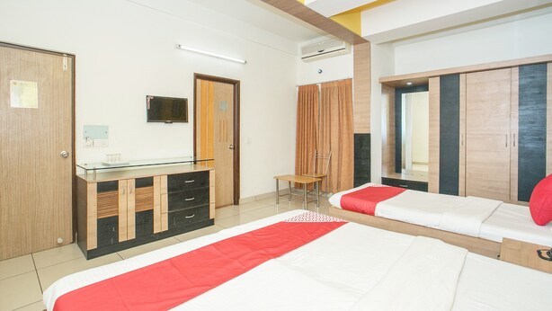 A hotel room with two beds, a TV, a wardrobe, and a desk with drawers. - OYO 8501 Abhimaani Comforts (Bengaluru)