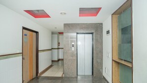 A hallway with a wooden door, a marble wall, and a glass elevator. - OYO 8501 Abhimaani Comforts (Bengaluru)
