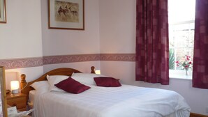 A neatly made bed with white and maroon pillows, a wooden headboard, a nightstand with a lamp, and a framed picture on the wall. - Garden Cottage & Granary (Ross-on-Wye)
