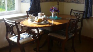A dining room with a round wooden table, six chairs, a vase of flowers, and a window with curtains. - Garden Cottage & Granary (Ross-on-Wye)