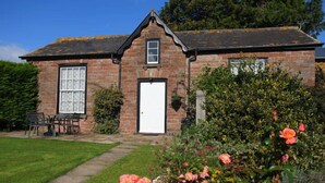 A brick house with a white door, a small window, and a garden with roses. - Garden Cottage & Granary (Ross-on-Wye)