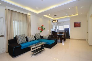 A modern living room with a sectional sofa, a glass coffee table, and a dining area with chairs and a table. - OYO Flagship 674 HSR Layout (Bengaluru)