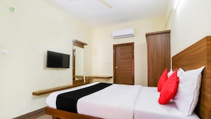 A hotel room with a bed, a flat-screen TV, a wooden wardrobe, and an air conditioning unit. - OYO 9253 Champion Comfort (Bengaluru)
