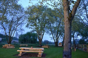 Un espace pique-nique avec des bancs et des tables en bois, entouré d’arbres.
