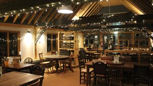A cozy restaurant with wooden tables and chairs, string lights, and a bar area.