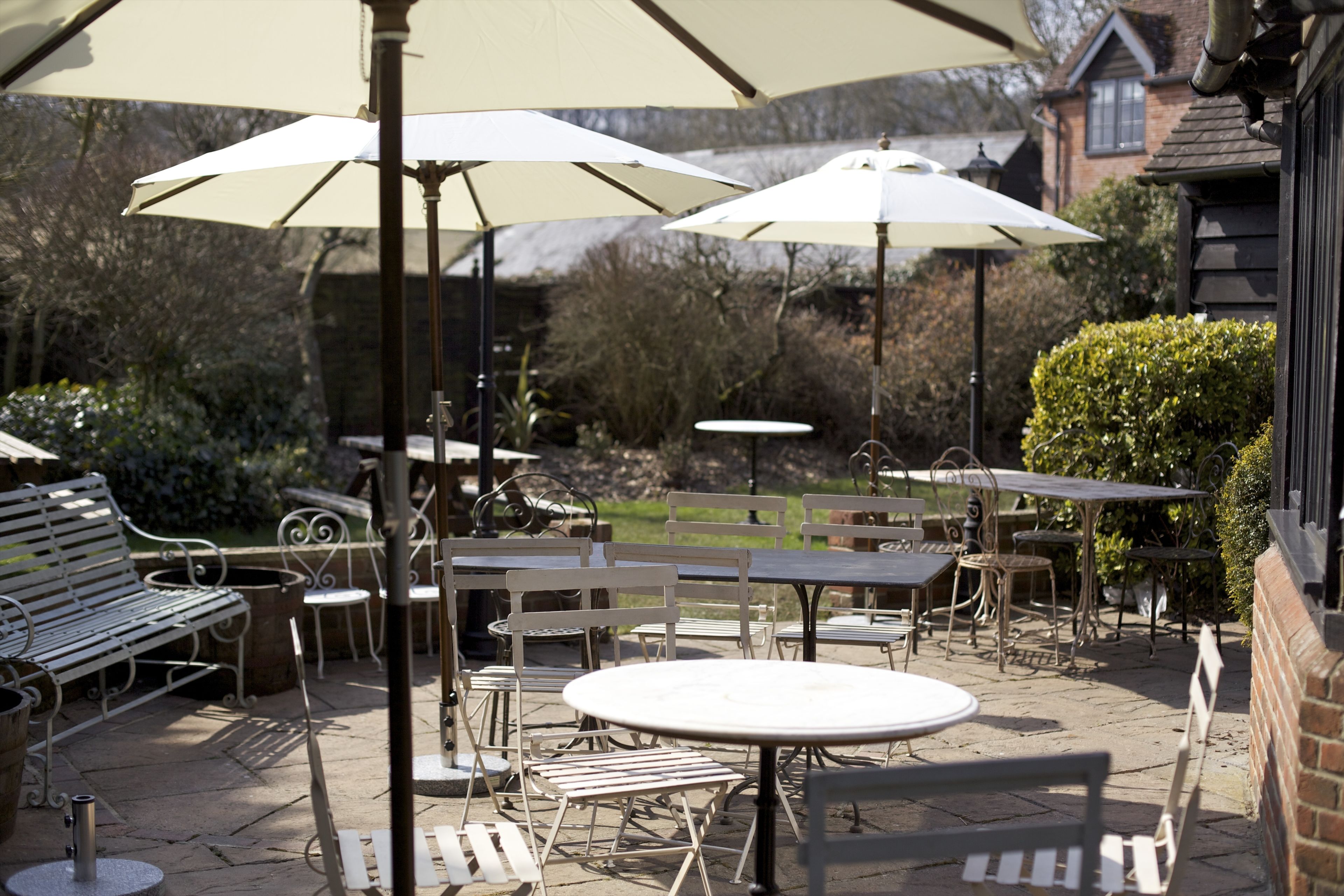 An outdoor patio with tables and chairs, umbrellas, and a bench.