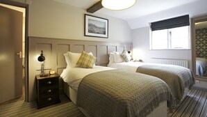A hotel room with two beds, a nightstand with a lamp, a framed picture on the wall, and a window with a view.