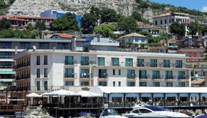 A multi-story hotel with balconies, a terrace with umbrellas, and a view of the sea and surrounding buildings. - Mistral Hotel (Balchik)