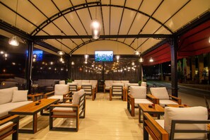 A modern lounge area with sofas and tables, a large TV screen, and a curved ceiling structure. - Mistral Hotel (Balchik)