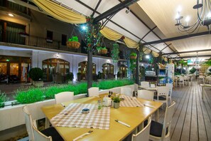 An outdoor dining area with checkered tablecloths, white chairs, and hanging plants. - Mistral Hotel (Balchik)