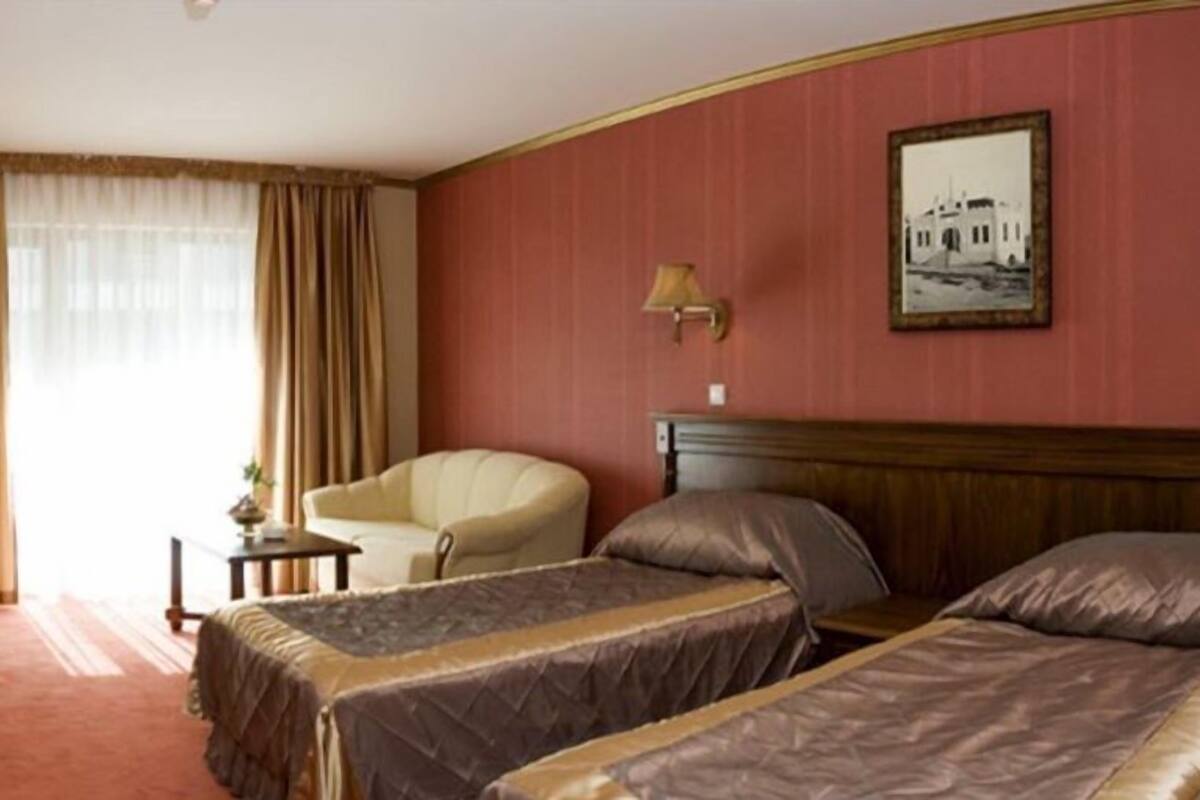 A hotel room with two single beds, a chair, a small table, and a lamp.